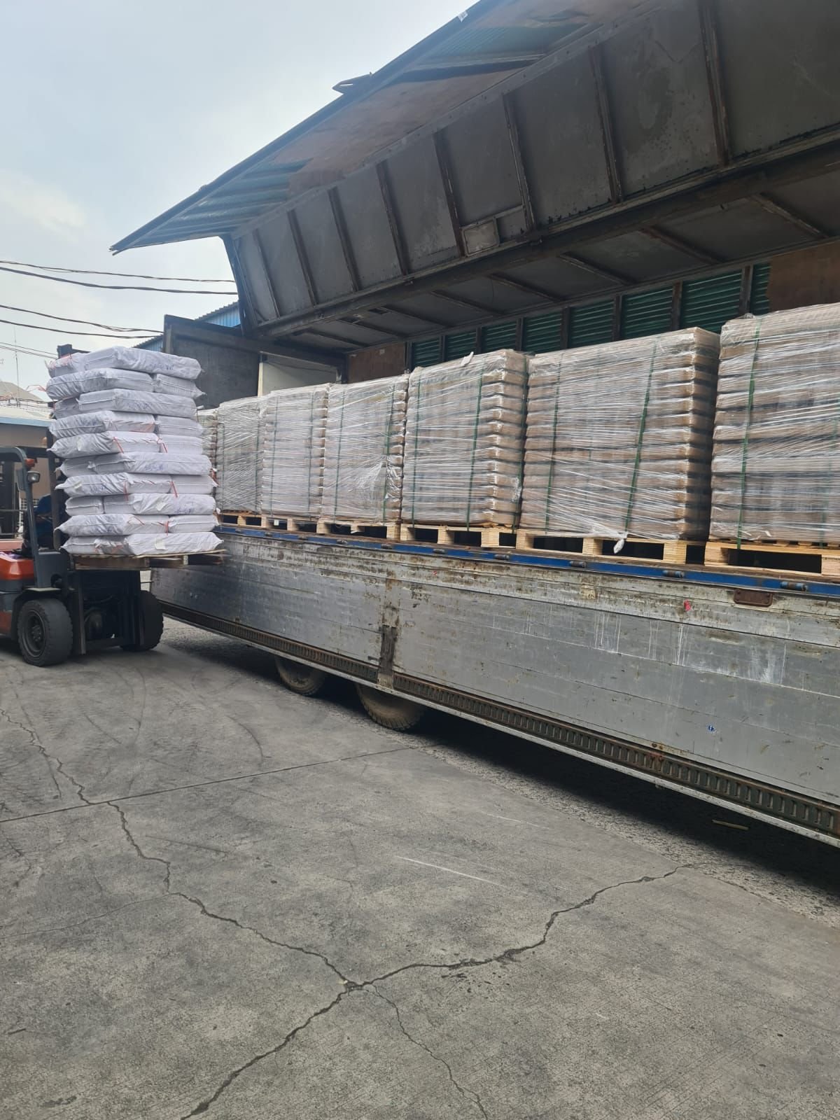 Pengiriman kemasan kaca besar di truk dengan pallet di luar gudang.