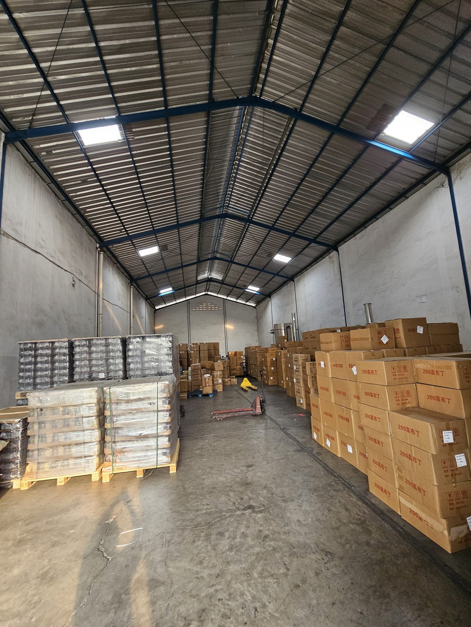 Interior gudang penyimpanan kemasan kaca dengan banyak kotak dan pallet.